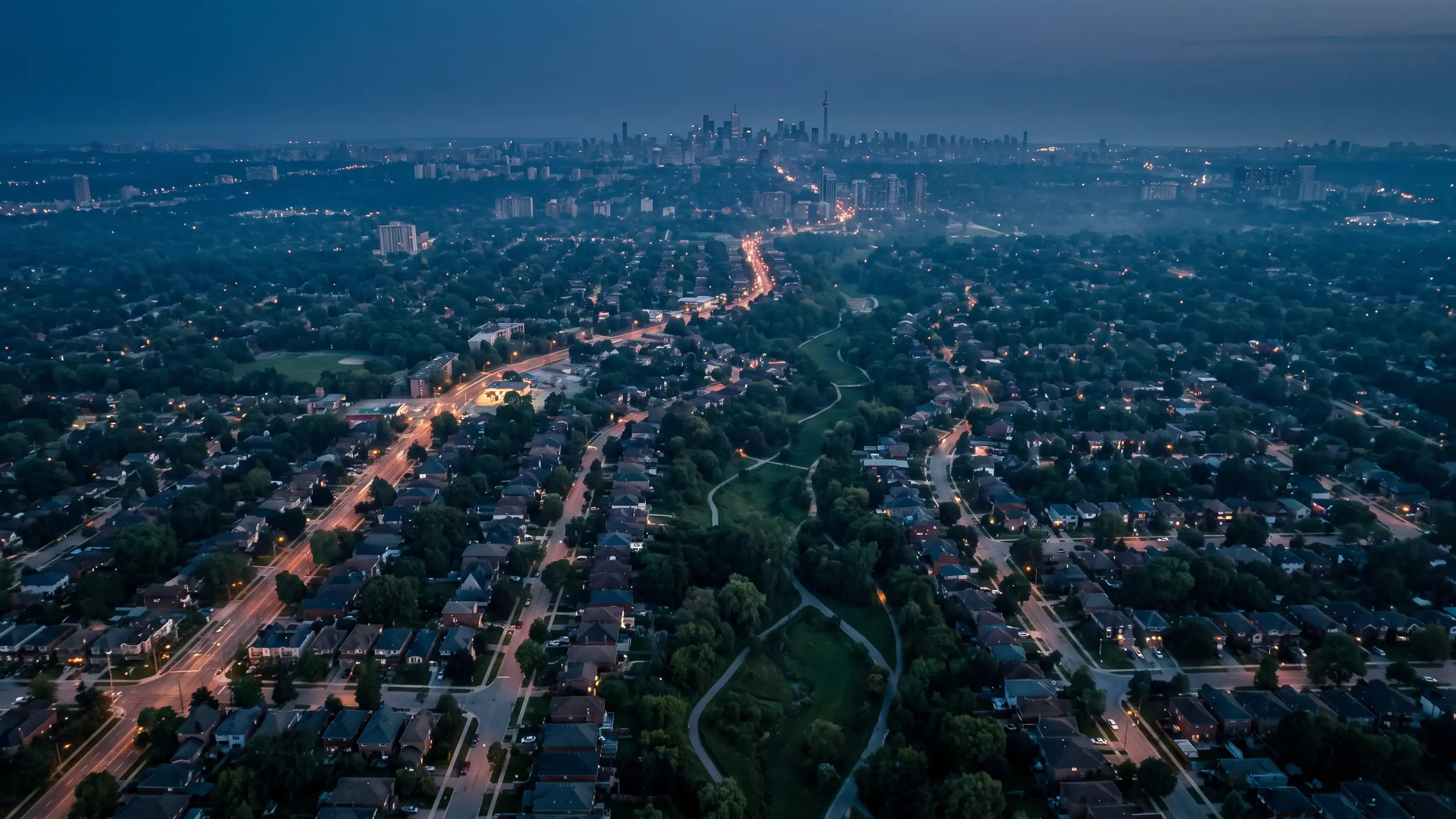 Aerial view across Toronto's residential neighbourhoods at dusk, with the downtown skyline on the horizon